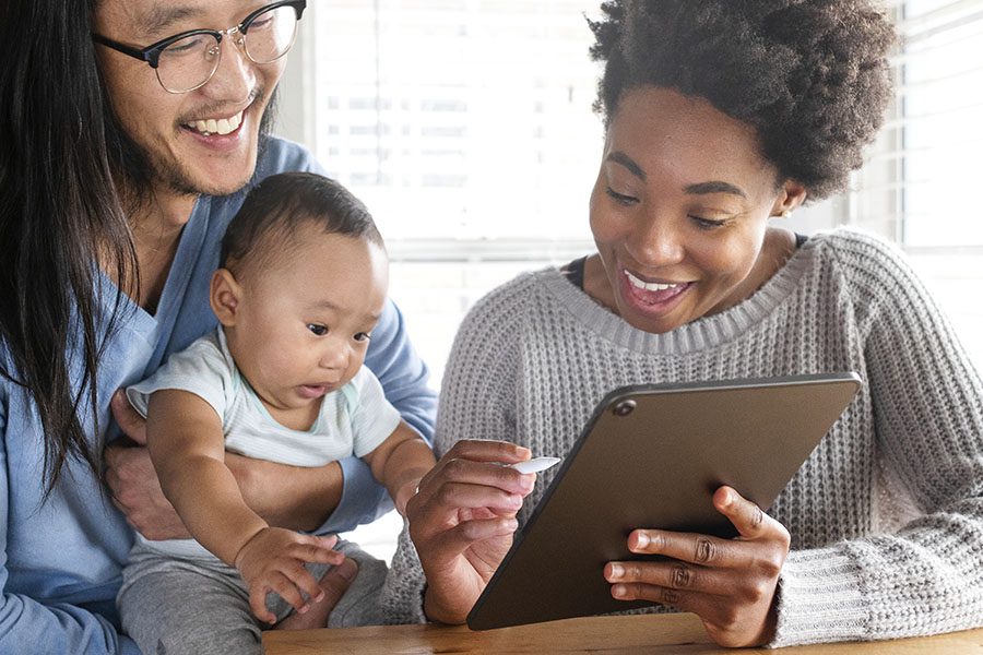Client Center - Cheerful Young Couple Holding Their Baby While Using a Tablet at Home