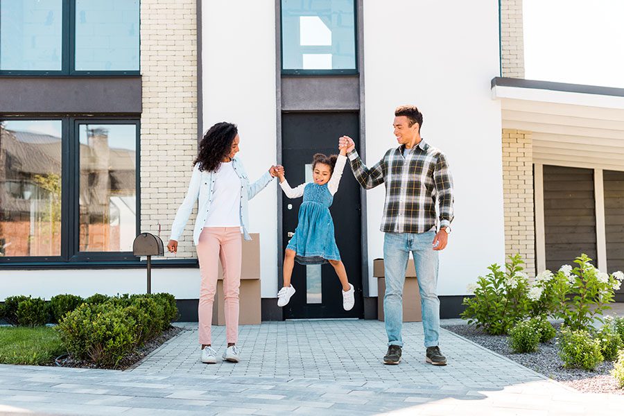 Home and Auto Insurance - Portrait of Happy Parents Holding Up Their Daughter in the Air While Standing Outside Their New Home on a Sunny Day