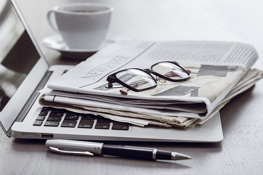Agency News - Desk with Coffee and Laptop with Newspaper and Glasses Sitting on Top